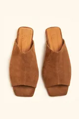 Sandalia mule de gamuza marrón, de una sola pieza con diseño asimétrico, punta cuadrada y suela plana.