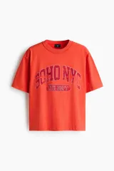 Remera de algodón en color rojo, con cuello redondo acanalado, mangas cortas y hombros caídos. Presenta un estampado frontal con la leyenda "SOHO NYC ATH DEPT".