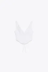 Top blanco tipo corsetero con escote pico y tirantes anchos. Detalle de bordados perforados a tono. Abertura en espalda ajustable con lazadas.