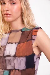 Musculosa de cuello redondo con volados en las sisas y diseño estampado de bloques estilo patchwork en tonos marrones, blancos, celestes y violetas.