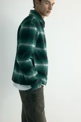 Sobrecamisa de lana con acabado cepillado, diseño a cuadros en tonos verde oscuro, negro y blanco. Cuenta con cuello inglés, cierre bidireccional frontal y bolsillos laterales discretos. Forrada y de corte regular.