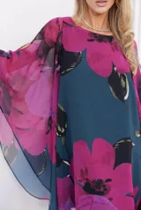 Vestido corto de corte amplio y fluido, con mangas tipo capa y escote redondo. Presenta un estampado floral de grandes flores fucsias sobre un fondo azul oscuro.