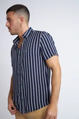 Camisa de manga corta con diseño a rayas verticales en color azul marino y blanco. Presenta cuello clásico, cartera abotonada frontal y logo bordado en el pecho. Posee un corte slim fit.