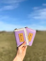 Billetera pequeña con cierre metálico, cuerpo principal de cuero lila texturizado y ribetes en color crema. Presenta un parche de cuero marrón con la palabra "chowie" escrita en cursiva.