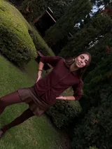 Blazer color borgoña con cuello, solapa y cuatro botones en el delantero. Tiene volados de encaje negro en cuello y delantero, manga larga con pliegues y bolsillo plaquet.