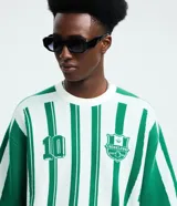 Remera de punto manga corta con diseño rayado vertical en color verde y blanco. Presenta cuello redondo, sisa desplazada y detalles gráficos tipo jersey de fútbol con el número 10 y el logo de la marca Reckless en el frente.
