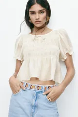 Blusa color beige, de mezcla de lyocell, con escote redondo, mangas cortas abullonadas y busto fruncido con tiras decorativas.