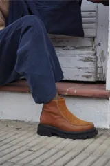 Bota corta de cuero color marrón con paneles en gamuza al tono, diseño de punta redondeada y suela track negra de goma. Presenta cierre lateral y detalle de costuras a la vista.