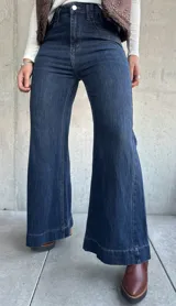 Jean de corte oxford con tiro alto, confeccionado en denim azul oscuro con costuras a tono. Presenta un diseño de pierna ancha y cierre frontal con botón metálico.