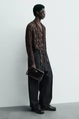 Bolso de mano tipo sobre color marrón oscuro, confeccionado en cuero. Cuenta con cierre de solapa con broche metálico dorado y asa de mano.