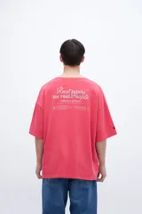 Remera de algodón teñida en prenda, color coral/rosado, con calce boxy y estampado en la espalda con texto en tipografía cursiva y líneas de texto más pequeñas.