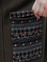 Buzo tipo campera de algodón orgánico color verde militar, con cierre frontal de botones a presión, capucha forrada con estampado étnico y bolsillos frontales con detalles de tejido aguayo multicolor.
