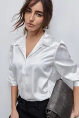 Camisa blanca de calce relajado con acabado satinado y brillo sutil, cuello clásico, cierre frontal con botones y mangas largas con puños.