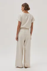 Pantalón de lino color beige, de pierna ancha, con botón en la cintura, pinzas en el frente y bolsillos delanteros y traseros.