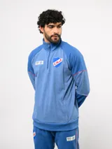 Buzo deportivo de medio cierre marca Umbro del Club Nacional de Football. Presenta un diseño en tonos azul y gris jaspeado, con cuello alto, mangas largas y detalles de costuras en contraste. Incluye el escudo del club y logo de la marca en el pecho.
