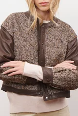 Chaqueta bomber color bordó con mangas de cuero sintético marrón y cuerpo de tweed con patrón de espiga. Cierre frontal con botones a presión y cuello redondo.