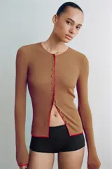 Chaqueta de punto marrón con cuello redondo, manga larga y ribetes en color rojo. Cuenta con cierre frontal de botones.