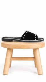 Sandalia plana de cuero negro con acabado gamuzado, tira ancha decorada con tachas metálicas plateadas y suela baja con borde pespunteado.