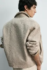 Cazadora de corte regular confeccionada en tejido de algodón con textura jacquard floral. Presenta cuello solapa, manga larga, cierre frontal con botones y bolsillos laterales de vivo.