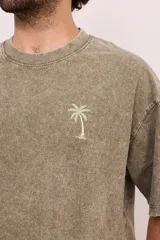 Remera negra con efecto gastado, corte oversize, mangas cortas y estampa en la espalda con palmeras, ángel en una hamaca y texto "Paradise Holiday Brixton".
