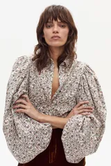 Camisa de manga larga con estampado floral en tonos crema, marrón, rosa y azul. Presenta cuello clásico y un corte que parece ser ajustado o con volumen en las mangas.