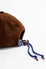 Gorra marrón de textura gamuzada con ojales bordados y visera curva, ajustable en la parte trasera.