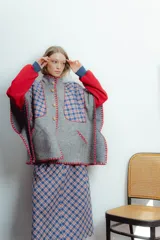 Poncho gris con diseño escocés en azul y rojo, cuello alto, cierre frontal con botones de madera y bordes con terminación crochet en rojo.