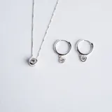 Conjunto de joyería compuesto por un collar con dije de punto de luz y un par de aros tipo argolla con dije colgante de punto de luz, ambos realizados en plata 925 con engarce inglés y circonias.