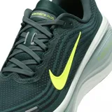 Championes de running Nike Vomero Plus, color verde oscuro con logo Nike Swoosh en amarillo neón. Presentan una suela gruesa con amortiguación visible que dice "ZOOMX".
