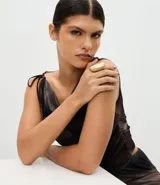 Maxi anillo de metal con baño de oro batido y diseño ovalado alargado. Presenta una abertura interna ajustable para mayor comodidad.