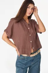 Camisa de lino marrón con mangas cortas, cuello mao con volados, cierre frontal con botones blancos y detalles de calados verticales en el frente.