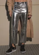 Pantalón de ecocuero metalizado color plateado, de corte capri semi oxford y tiro medio-alto. Presenta cierre frontal con botón metálico y costura horizontal a la altura de la rodilla.