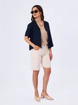 Bermuda de jean color beige, de tiro medio y corte recto, con bolsillos laterales y traseros, y presillas para cinto.
