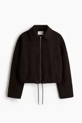 Campera corta marrón oscuro de mezcla de lana, con cuello camisero, cierre frontal plateado, bolsillos ribeteados y cordón ajustable en el bajo con dobladillo fruncido. Diseño oversized con hombros caídos y mangas largas.