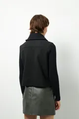 Tapado corto negro de paño con mangas y cuello tejidos, cierre metálico y bolsillos.