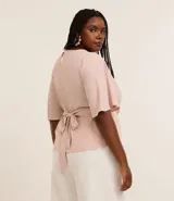 Blusa de crepé color rosa pálido, con cuello redondo, mangas cortas con volados, lazo en la cintura y botón en la espalda.