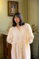 Vestido largo de muselina color crema, con silueta amplia y fluida. Presenta cuello en V, cierre frontal con botones y mangas largas relajadas.