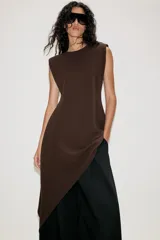 Vestido corto de color marrón, con cuello redondo y diseño sin mangas. Presenta un bajo asimétrico con un lateral más largo y cierre en la espalda con abertura y botón.