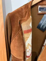 Campera de mujer combinada en lana merino y gamuza, color marrón. Presenta diseño tipo patch en el frente con paneles de gamuza con costuras visibles a contratono, cuello mao con cierre de botón a presión, mangas largas de punto acanalado y cierre frontal con cremallera.