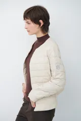 Campera acolchada tipo puffer en color beige, con diseño sin cuello y cierre frontal con botones a presión.
