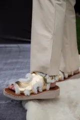 Sandalias con plataforma de madera y tiras de cuero color dorado con borde de corderito blanco.