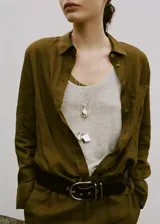 Camisa de lino color verde militar, de corte recto con cuello camisero, manga larga con puños abotonados, bolsillo de parche en el pecho y cierre frontal de botones.