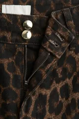 Pantalón de jean de tiro alto con pierna amplia y corte holgado, confeccionado en tela con estampado de leopardo en tonos marrón y negro. Presenta cierre y dos botones dorados en la cintura, y pliegues frontales.