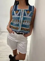 Chaleco corto en denim con bordado artesanal multicolor y escote cuadrado. Con cierre de botones y terminaciones desflecadas.