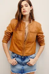 Saco corto de cuero ovino en color tostado, sin cuello, con detalles de trenzados en los bordes y bolsillos frontales con solapa.