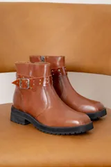 Bota corta de cuero color suela, con suela track negra, hebilla metálica lateral y detalle de tachas en la tira decorativa.