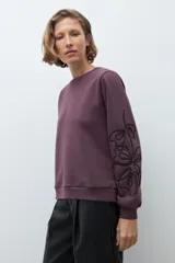 Sweatshirt color ciruela de cuello redondo y manga larga, con detalle de apliques bordados en relieve en las mangas.