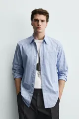 Camisa de corte regular fit confeccionada en tejido de algodón, con diseño de rayas verticales en tonos azules. Presenta cuello abotonado, manga larga con puños abotonados, cierre frontal de botones y un bolsillo en el pecho.