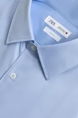 Camisa de manga larga, color blanco, con cuello italiano y corte slim fit. Presenta cierre frontal de botonadura y puños con botón.