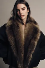 Chaqueta bomber negra de corte corto y diseño abullonado, con cuello de solapa amplio en pelo sintético marrón. Cuenta con mangas largas y cierre frontal.